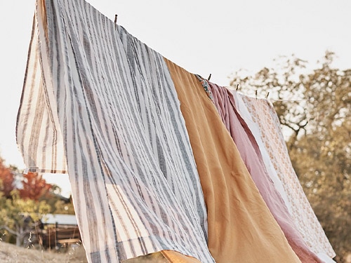 Solid and striped linen sheets drying on a line in a bright field.