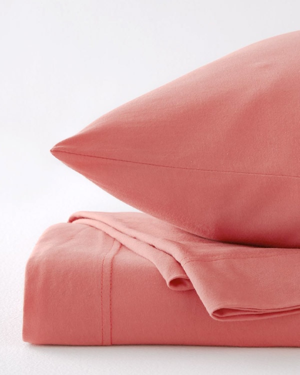 A close-up image of a pillow and a folded flat sheet, Jersey-Knit Sheets in Muted Clay.